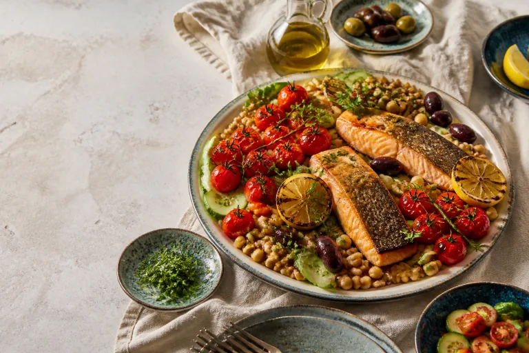 Grilled salmon with tomatoes, chickpeas, cucumber, olives, lemon and whole grains on a Mediterranean table.